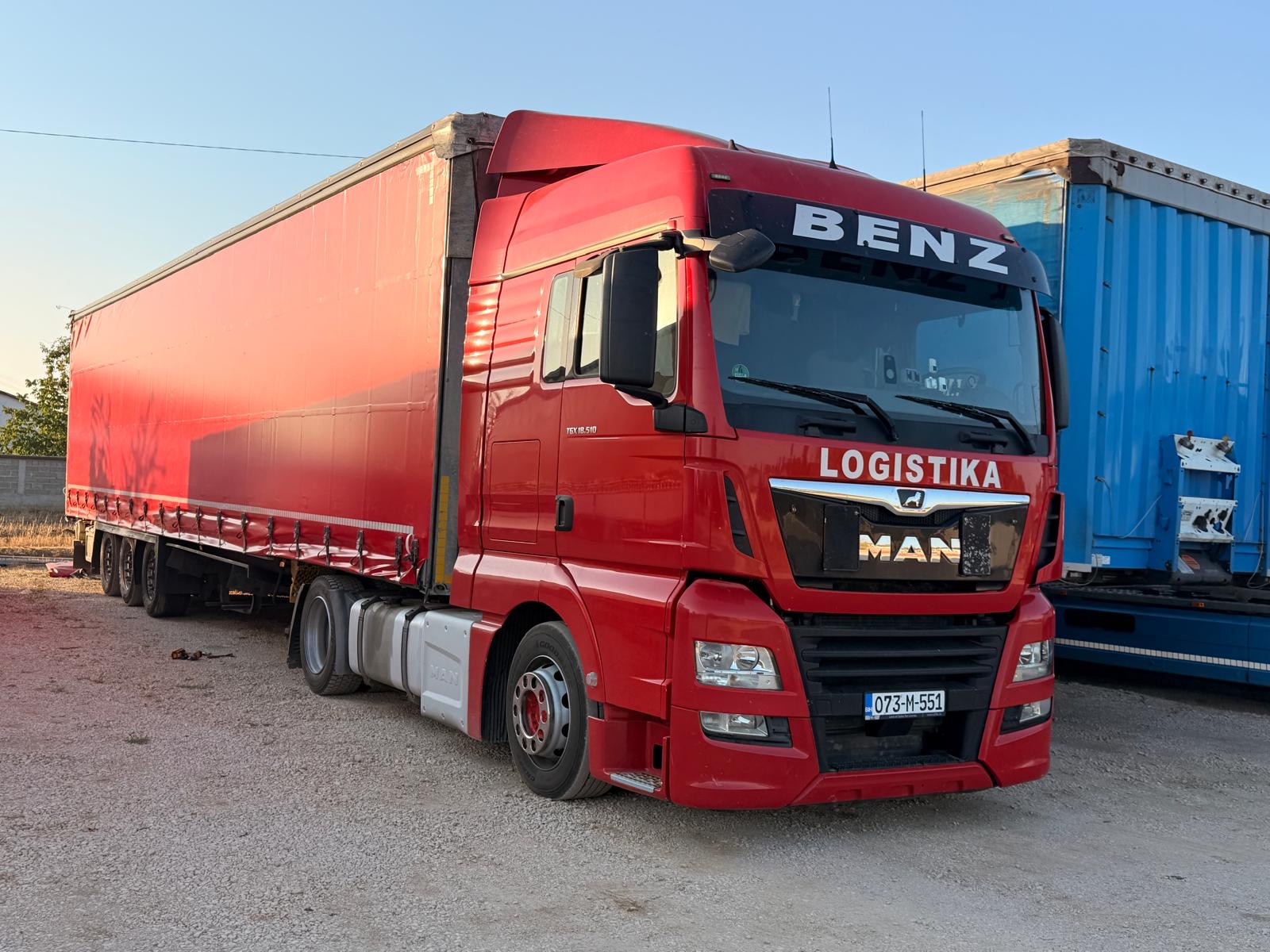 Crveni MAN kamion sa crvenom prikolicom BENZ LOGISTIKA na šljunku