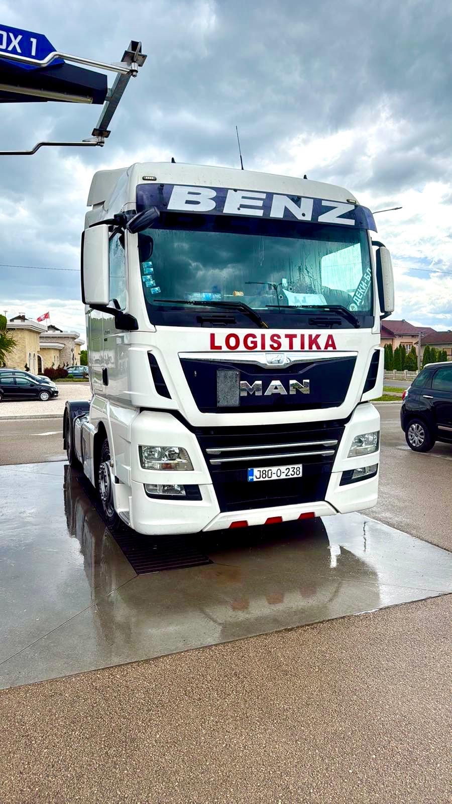 Bela MAN kabina sa crvenim LOGISTIKA natpisom na mokroj podlozi koja reflektuje nebo